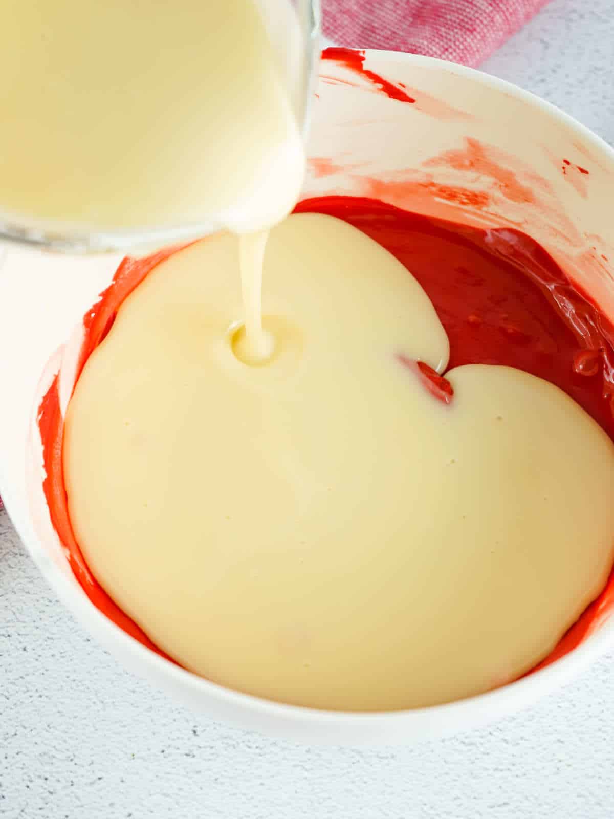 pouring melted buttercream frosting into melted red candy melts.