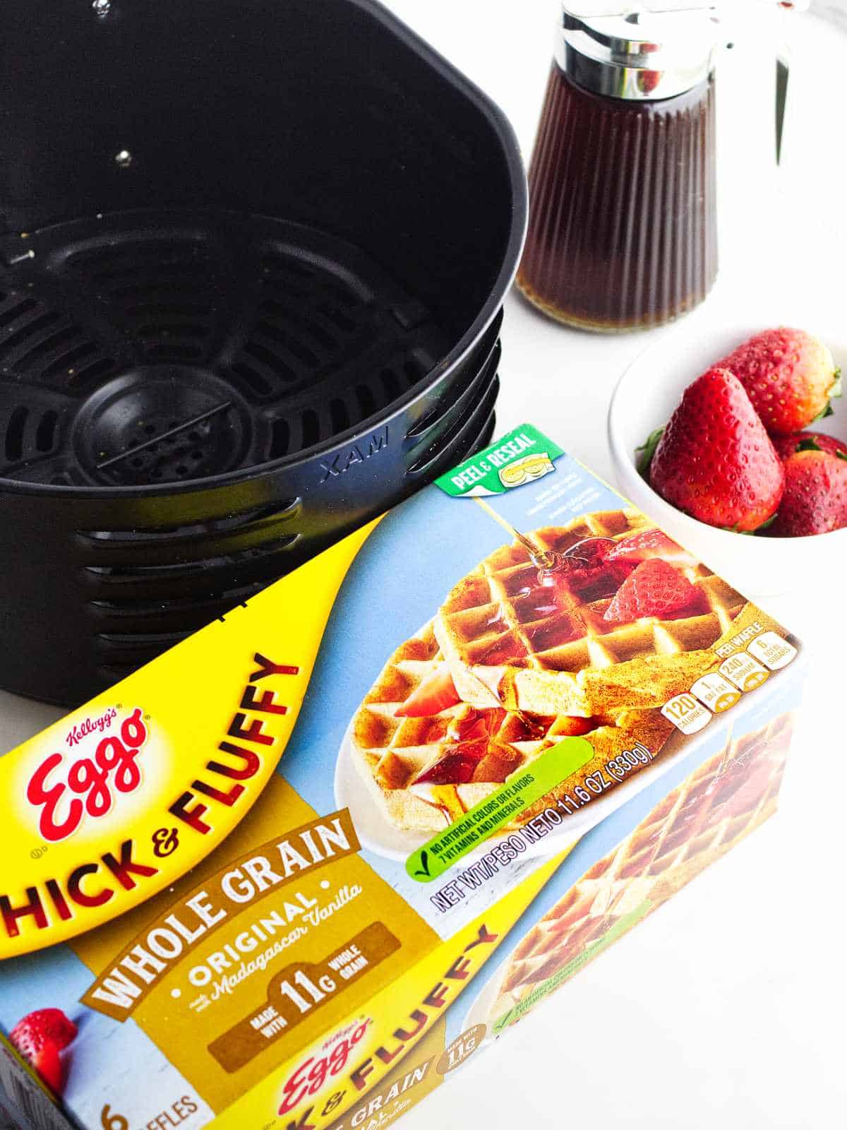 Eggo waffles, air fryer basket, strawberries, and maple syrup on a white background.