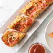pepperoni french bread pizza on a plate with marinara sauce nearby.