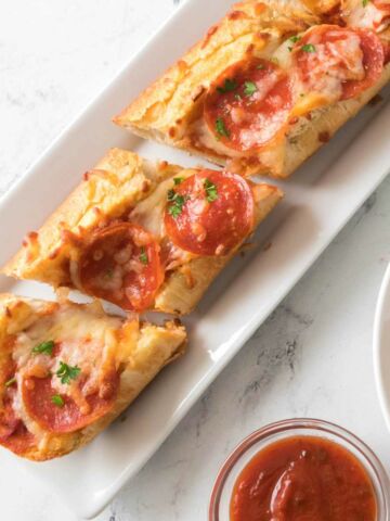 pepperoni french bread pizza on a plate with marinara sauce nearby.