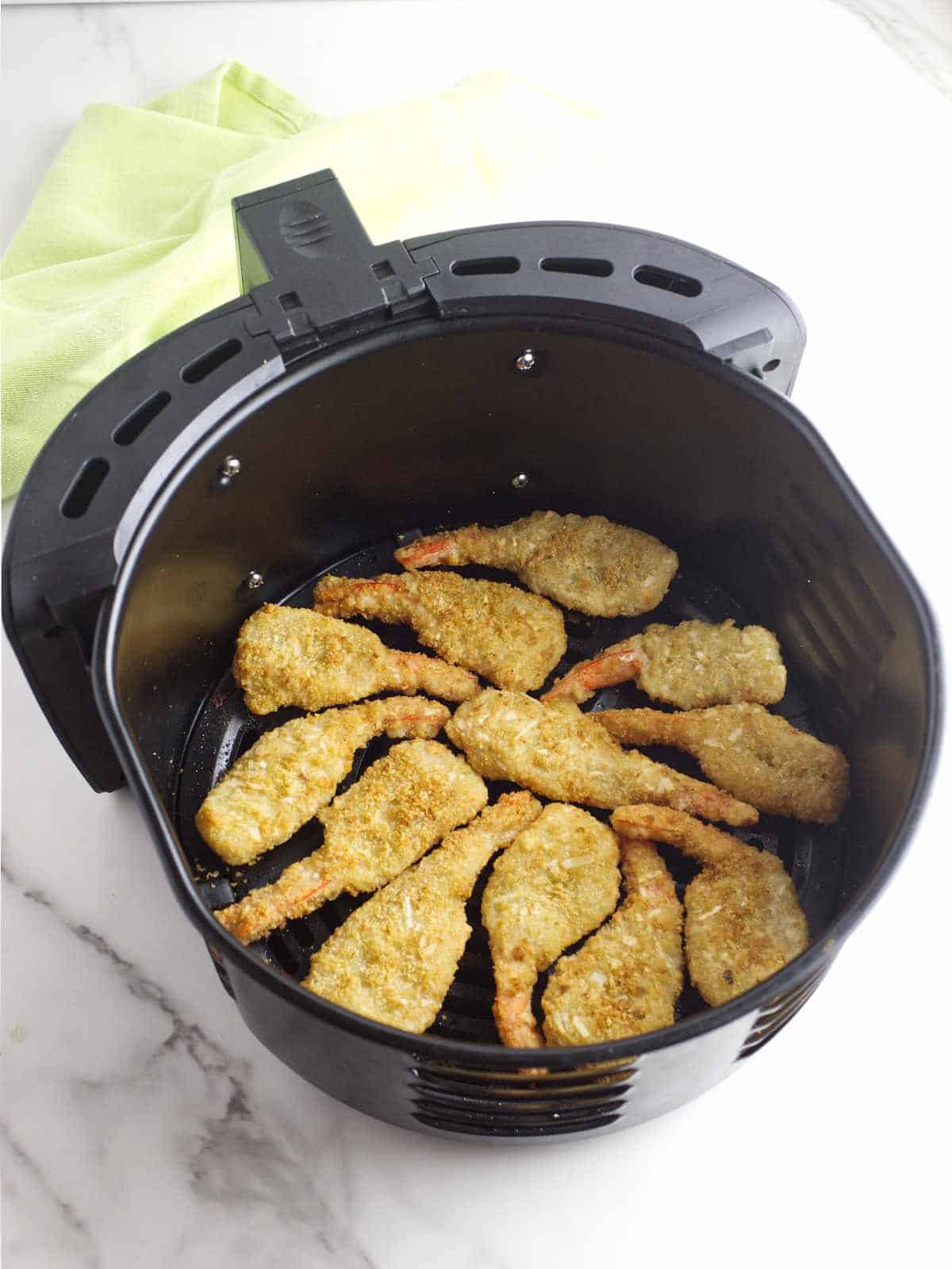 frozen coconut shrimp spread out in a single layer in air fryer basket.