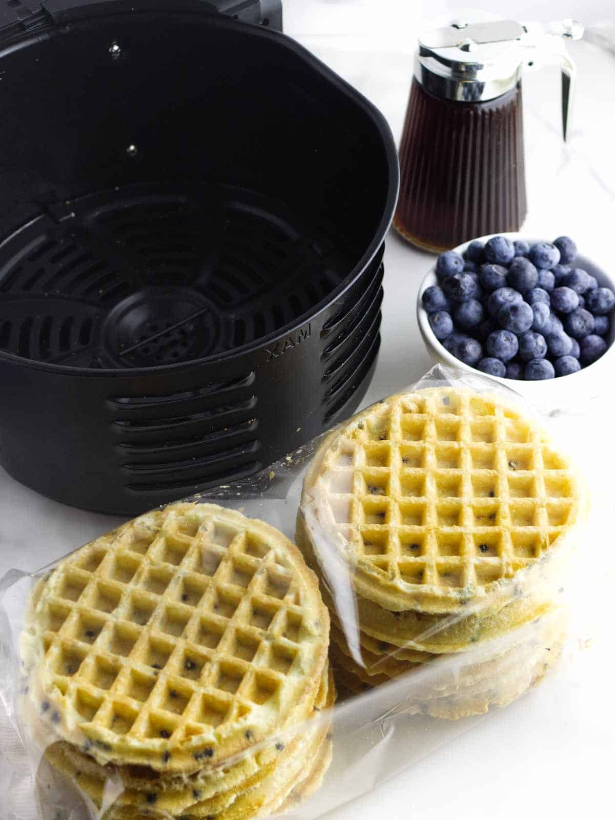 air fryer, frozen waffles, pitcher of maple syrup, and bowl of blueberries on a white background.