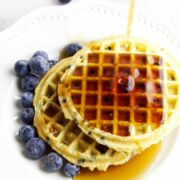 maple syrup being drizzled on air fryer frozen waffles on a plate with blueberries.