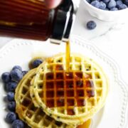 maple syrup being drizzled on air fryer frozen waffles on a plate with blueberries.