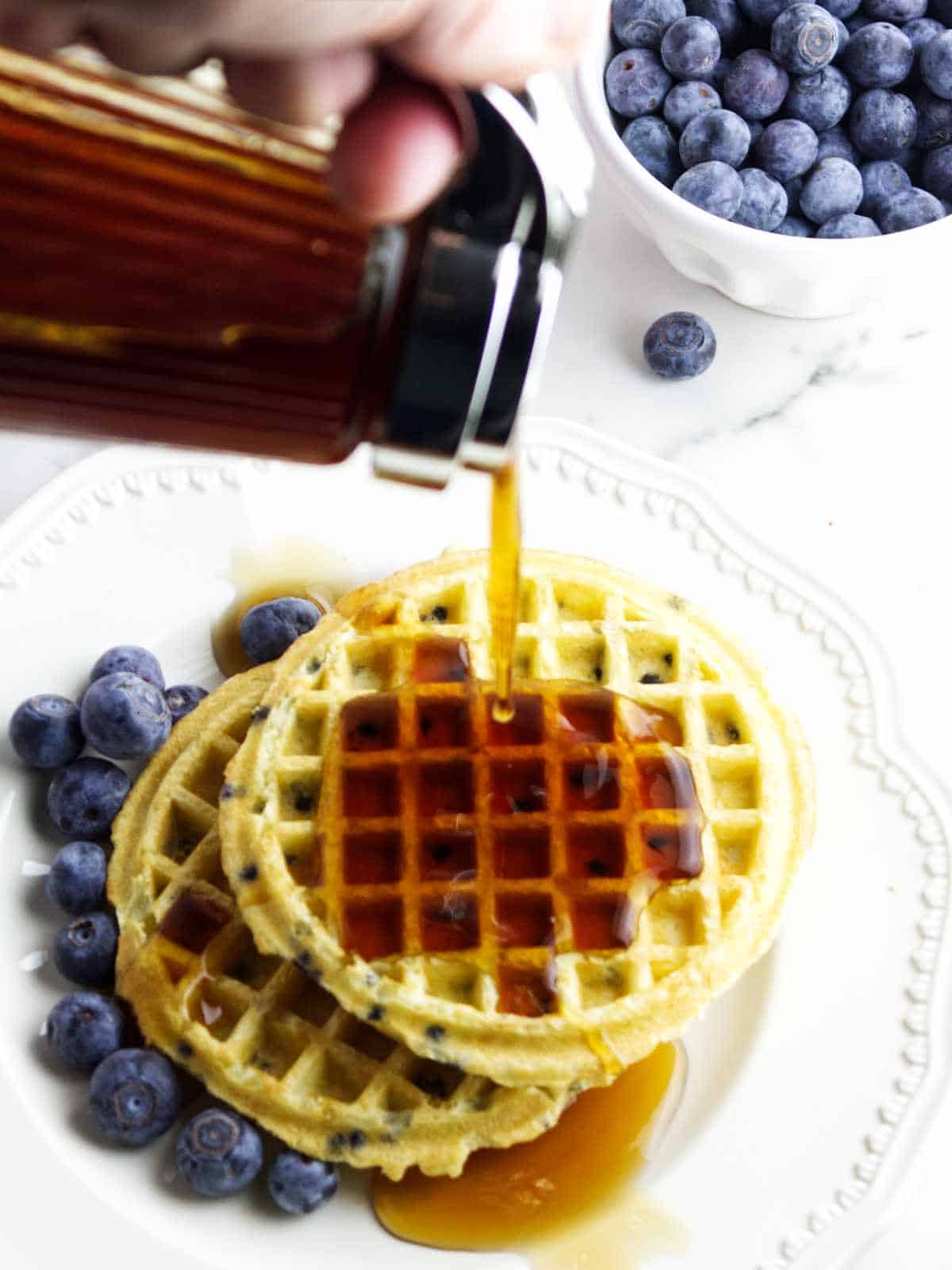pouring maple syrup on plate of waffles.