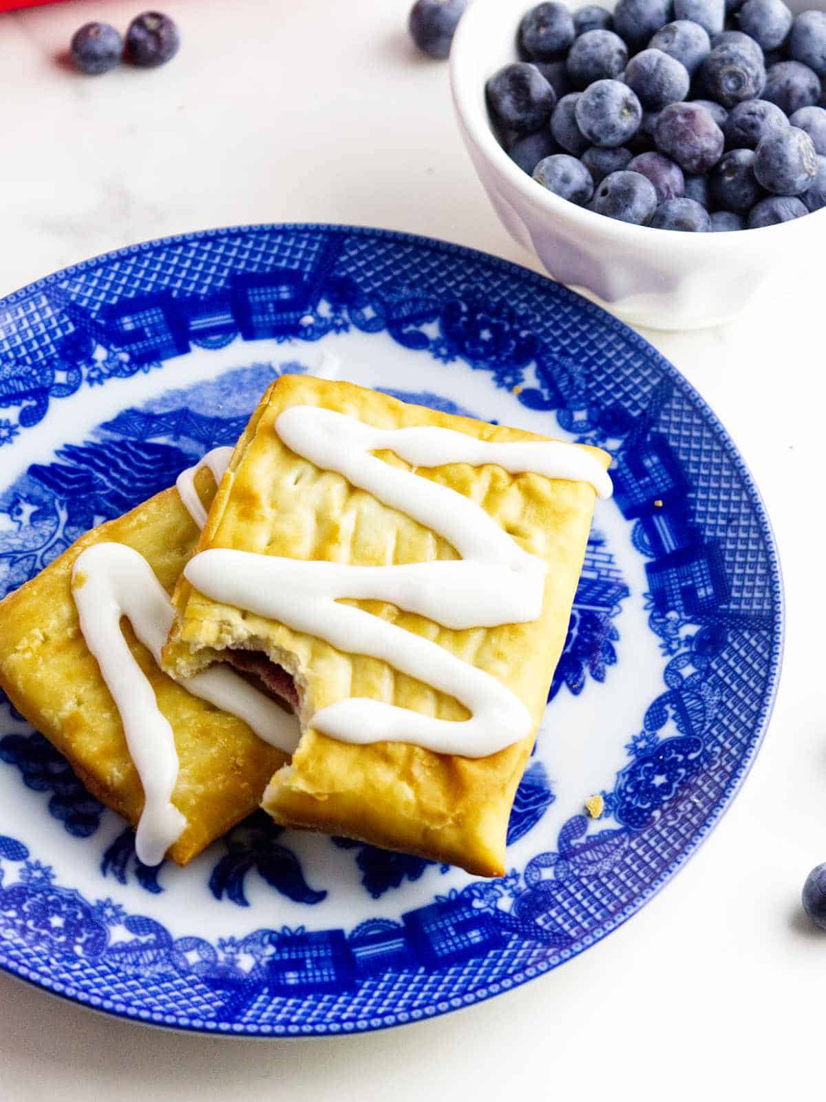 blue and white plate with iced golden brown pastries, and some blueberries on the white background.