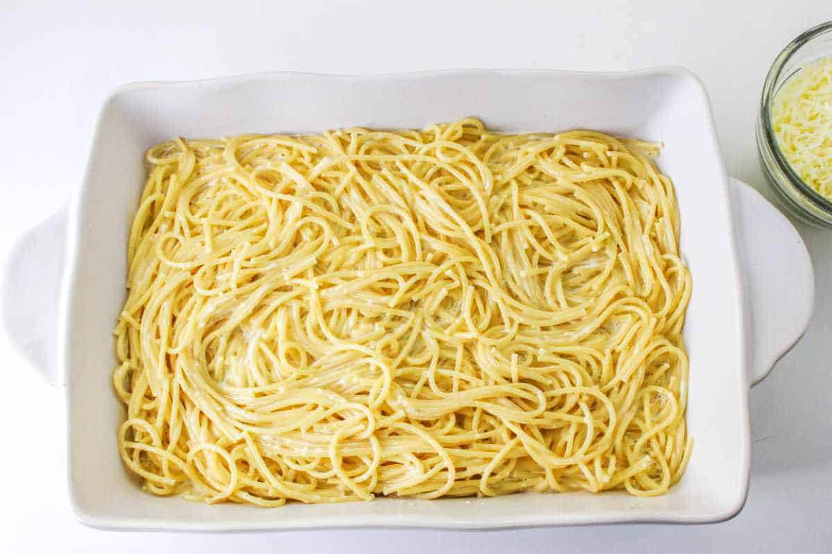 Alfredo sauce and cooked spaghetti noodles spread on bottom of a casserole dish.