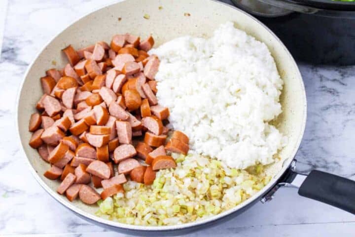 cubed sausage, cooked rice, and sauteed onions in a skillet.