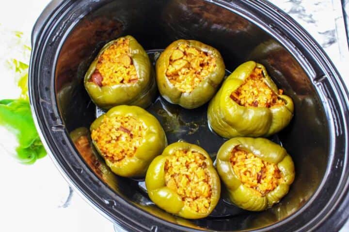 Six green bell peppers stuffed with rice and meat sit in a slow cooker, ready to be cooked.
