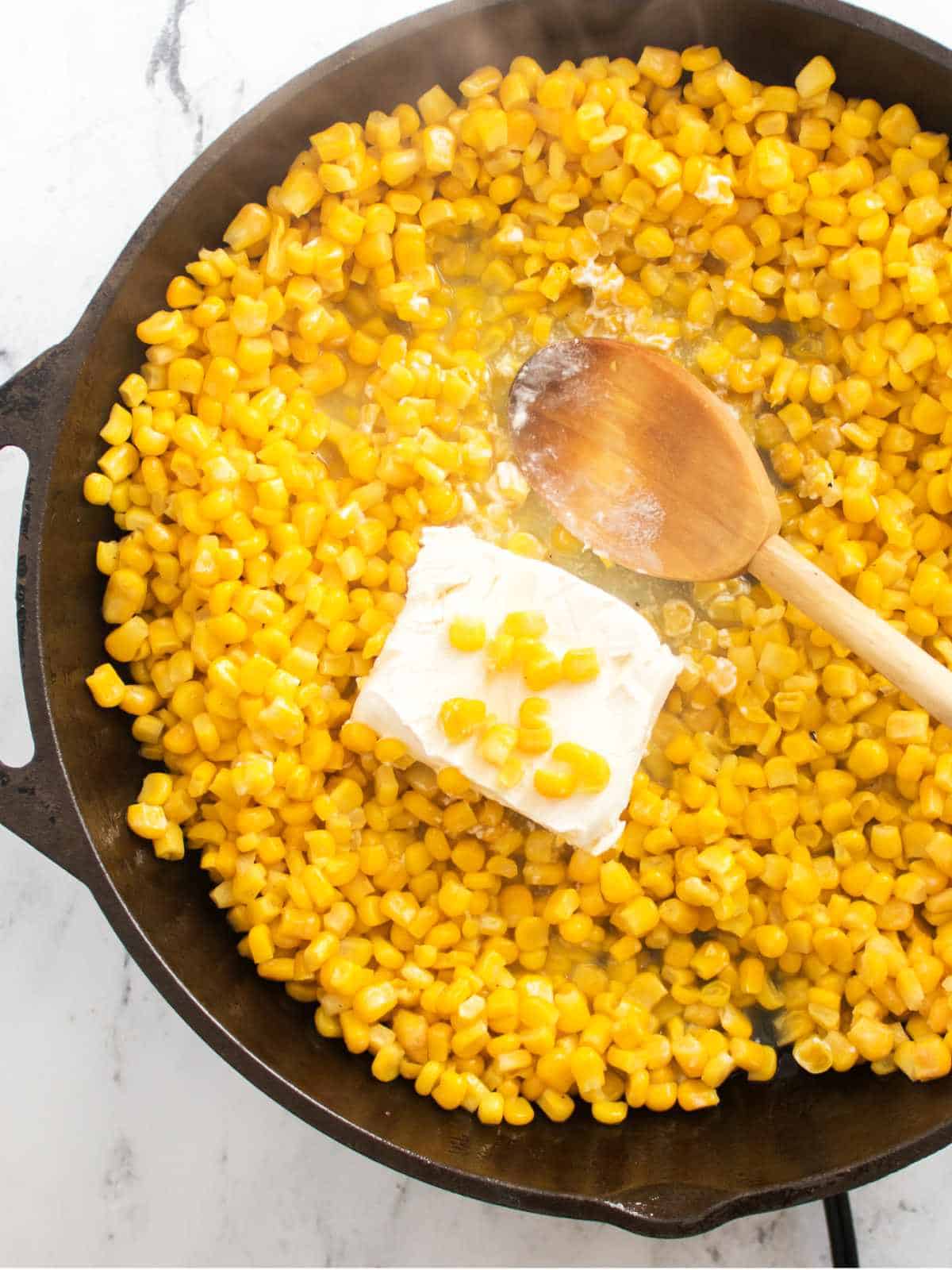 cream cheese melting in skillet of frying corn.