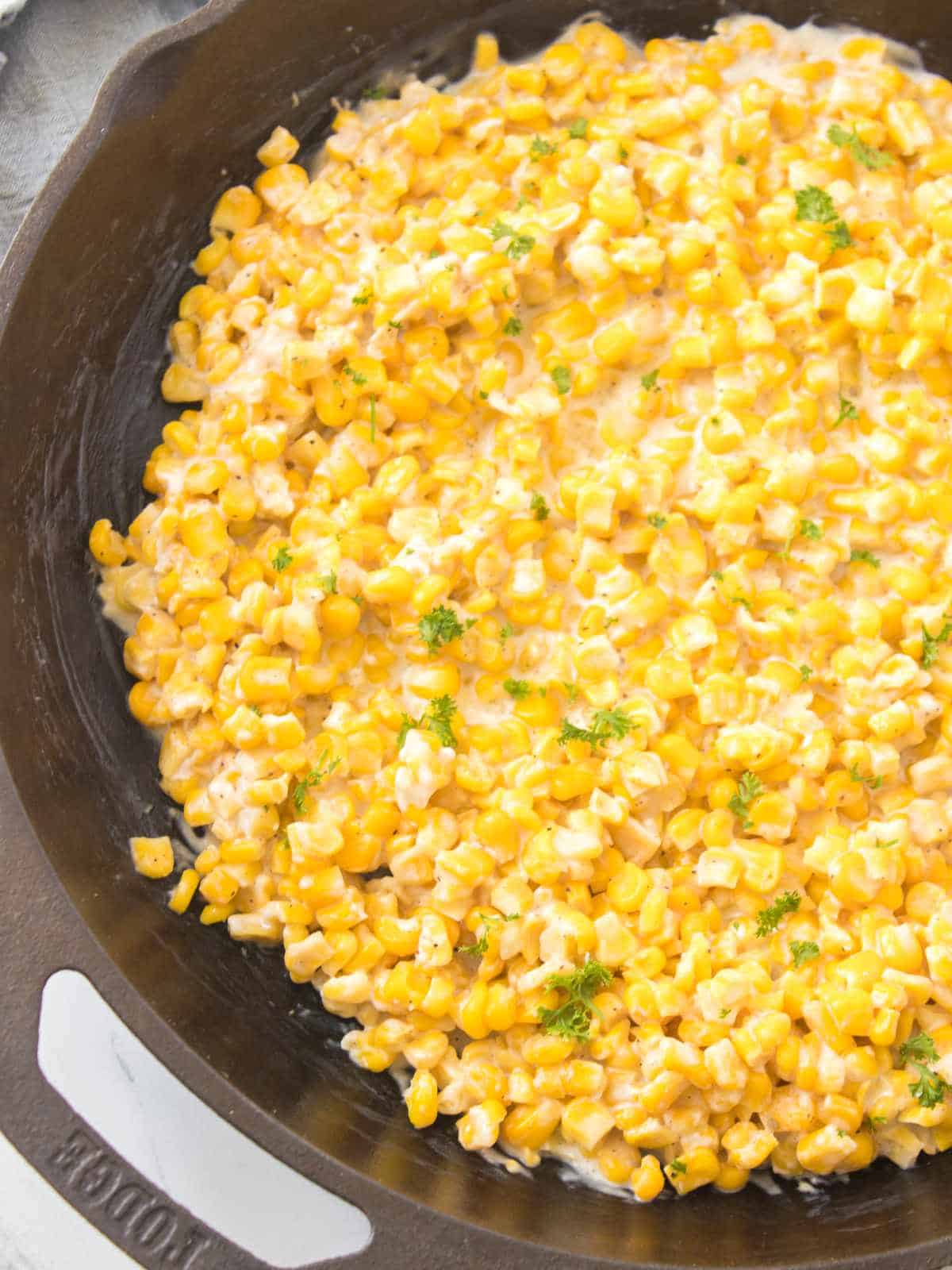 Creamy corn with spices and parsley garnish in a cast iron skillet.