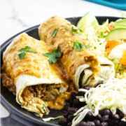 chile relleno burrito with salsa queso sauce on a platter of rice, lettuce, and black beans.