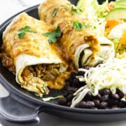 chili relleno burrito with salsa queso sauce on a platter of rice, lettuce, and black beans.