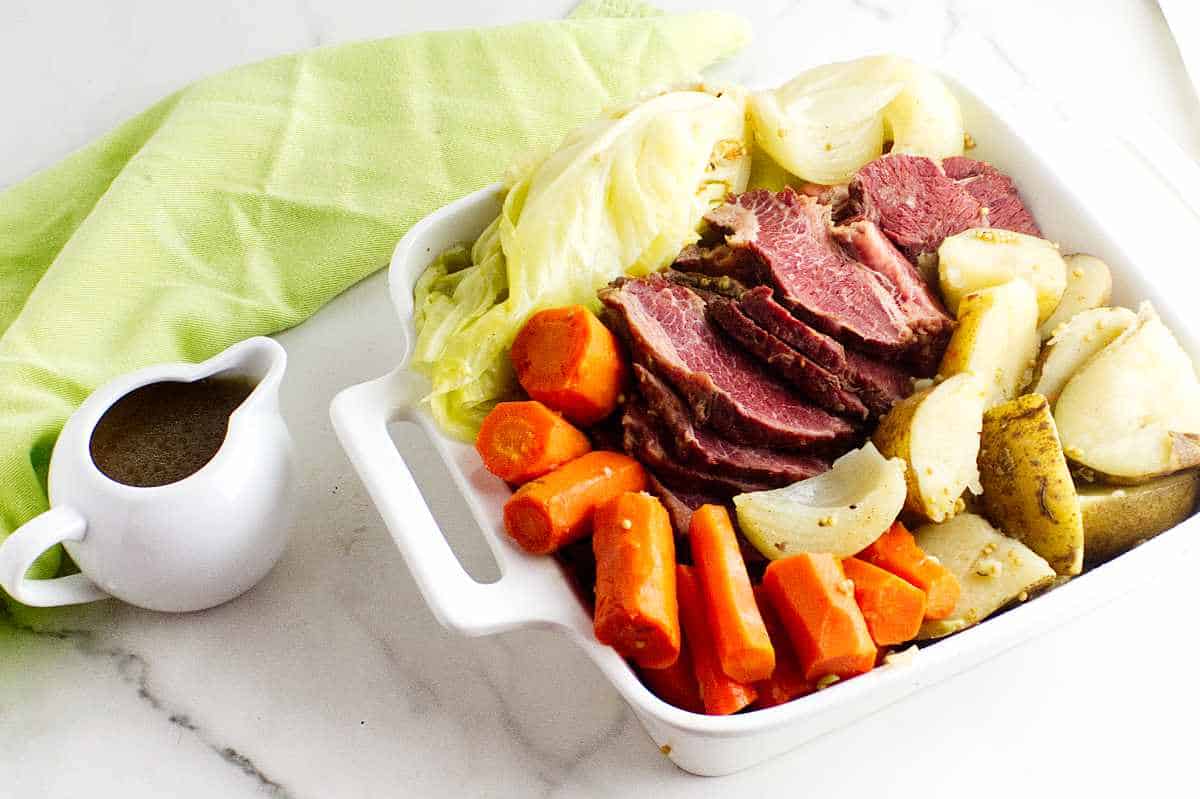Serving dish with sliced corned beef, carrots, potatoes, and cabbage.