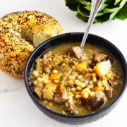 a bowl of beef and barley soup with a bagel side.