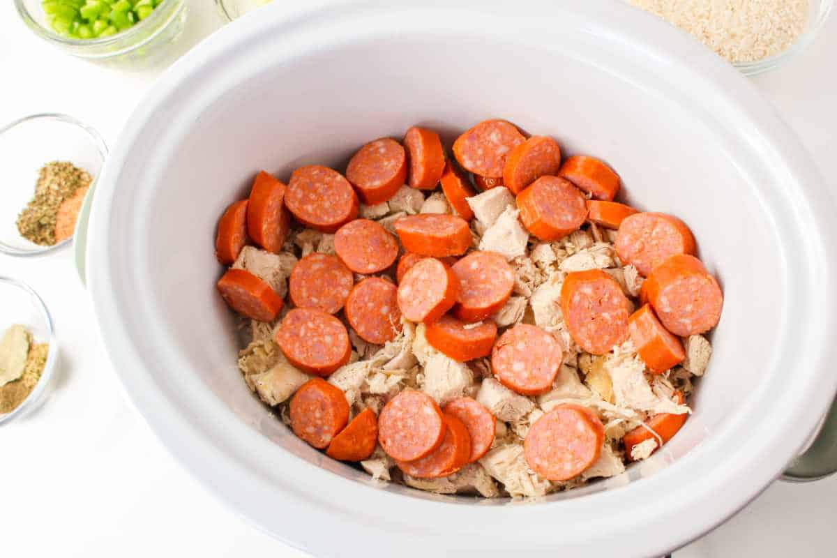 layers of chicken and sausage on the bottom of a slow cooker or dutch oven.