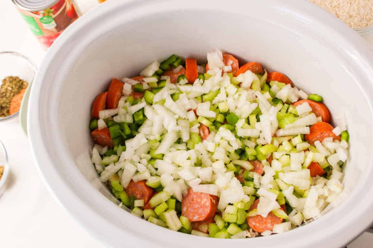 onions and bell peppers on top of sausage in a crockpot or dutch oven.