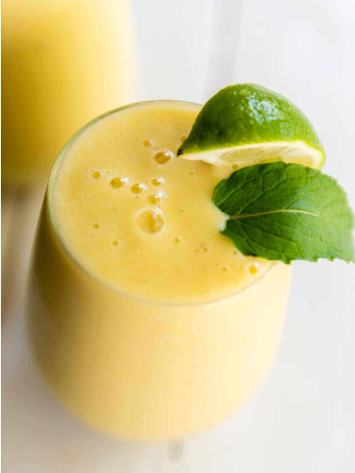 mango pineapple smoothie garnished with lime wedge and mint leaf.