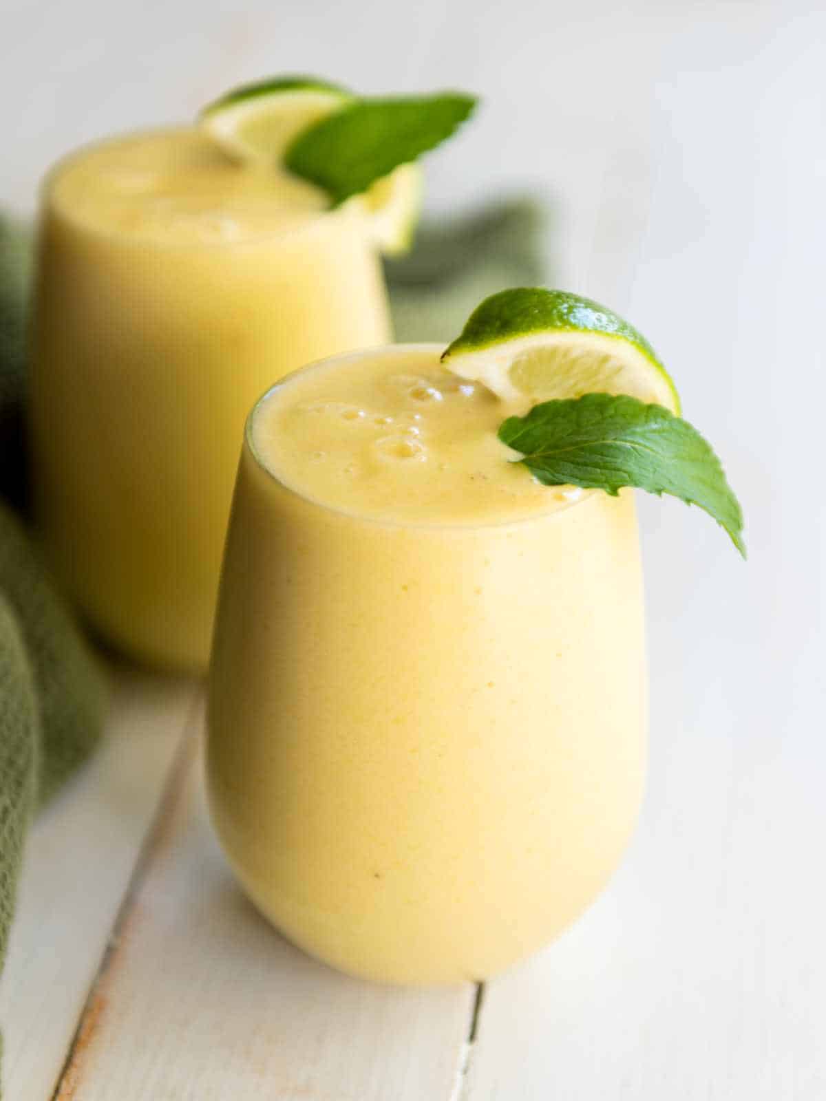 mango pineapple smoothie garnished with lime wedge and mint leaf.