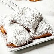 princess tiana's beignets covered with powdered sugar on a serving plate.