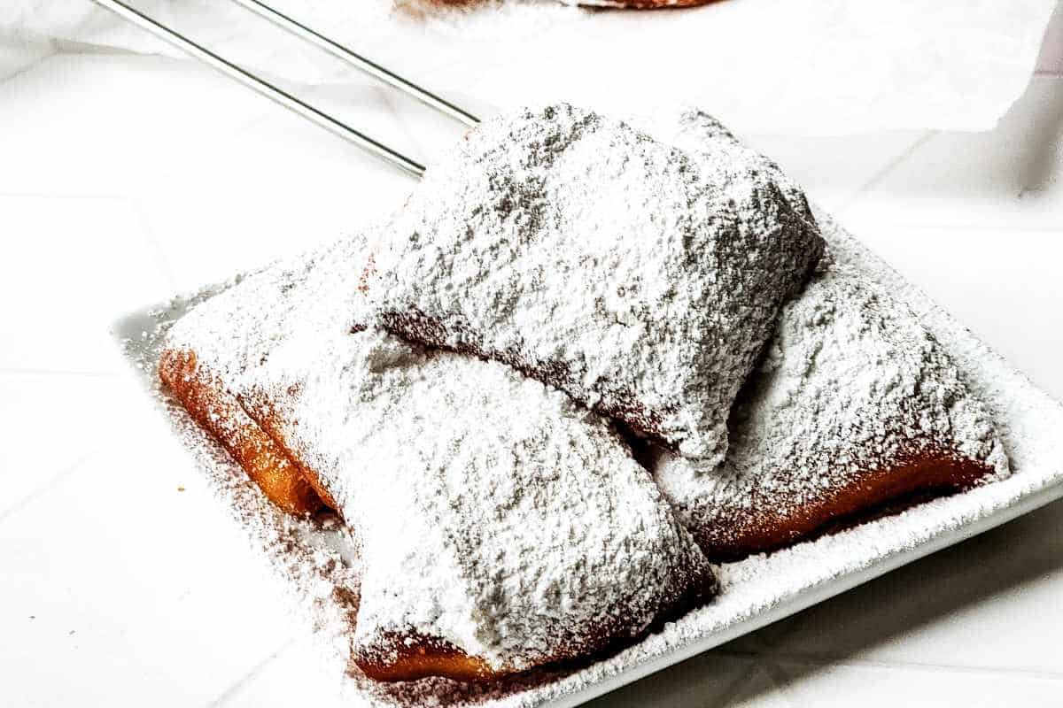 plate of fresh fried beignets on a plate and covered in powdered sugar.