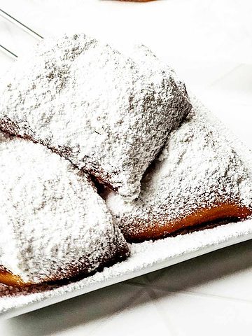 princess tiana's beignets covered with powdered sugar on a serving plate.