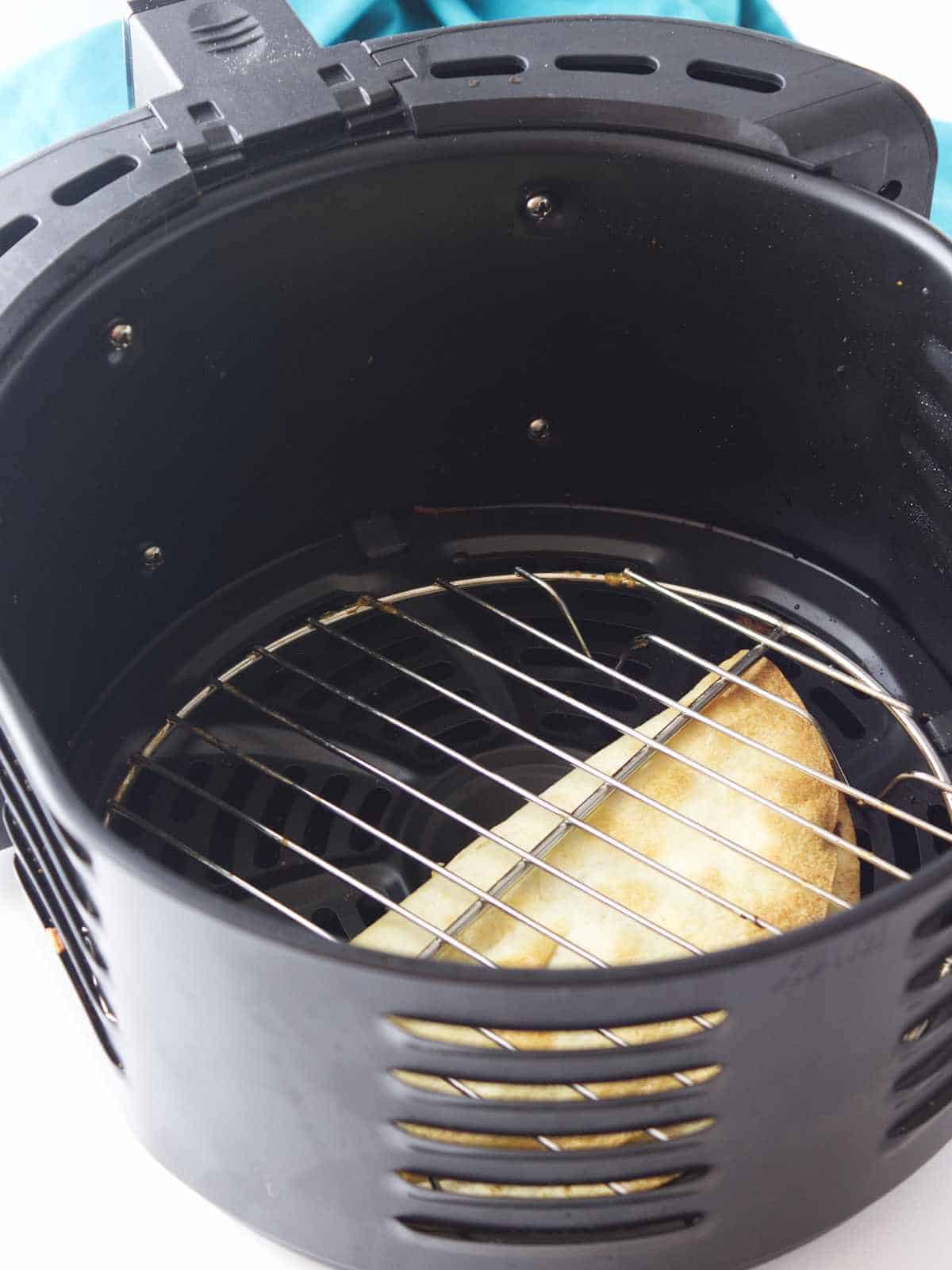 golden brown folded quesadilla in an air fryer with round rack as a weight.