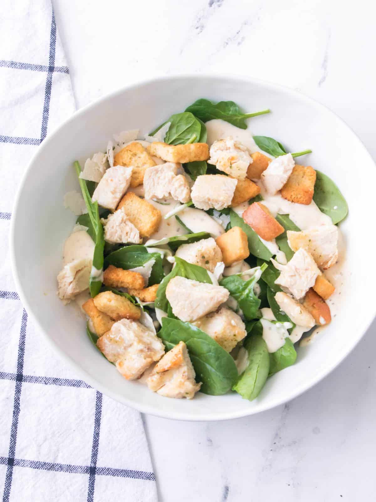 Bowl of Caesar salad with air fried chicken breast with croutons and shaved Parmesan cheese.