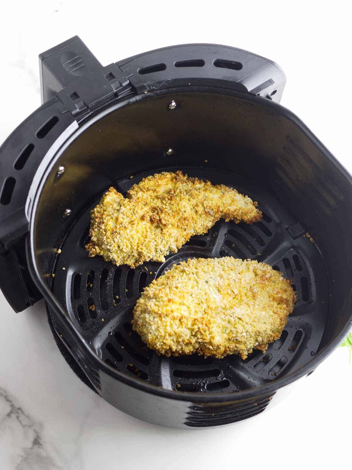golden crispy air fried chicken cutlets in an air fryer basket.