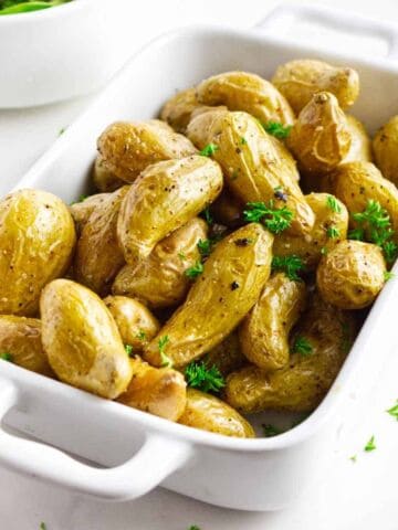 casserole serving dish filled with roasted fingerling potatoes garnished with parsley.