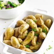 casserole serving dish filled with roasted fingerling potatoes garnished with parsley.