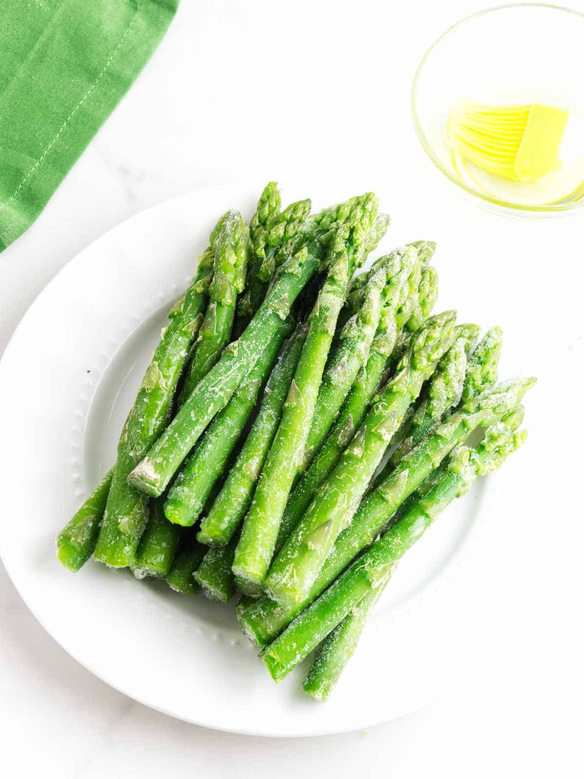 frozen spears of asparagus on a plate with a small bowl of olive oil nearby.