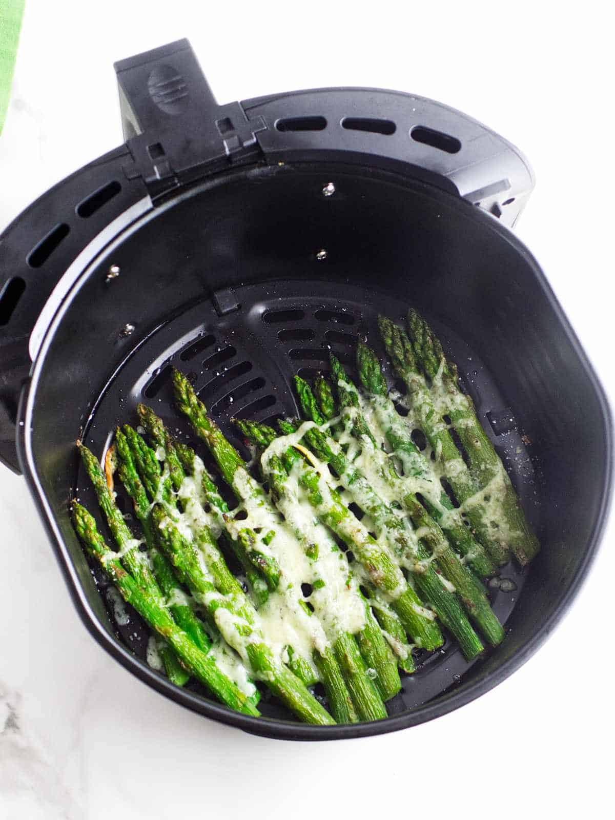 Air fryer basket with melted cheese on hot asparagus.