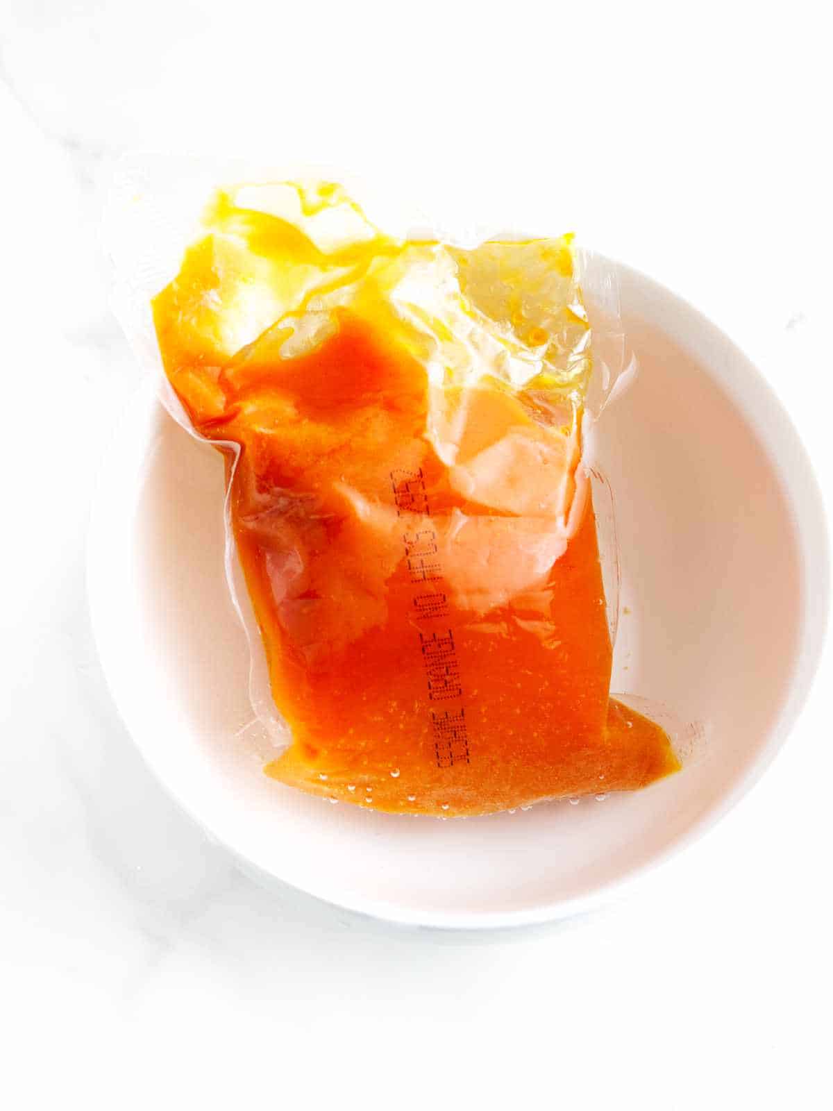 packet of orange citrus sauce in a bowl of hot water on a white background.