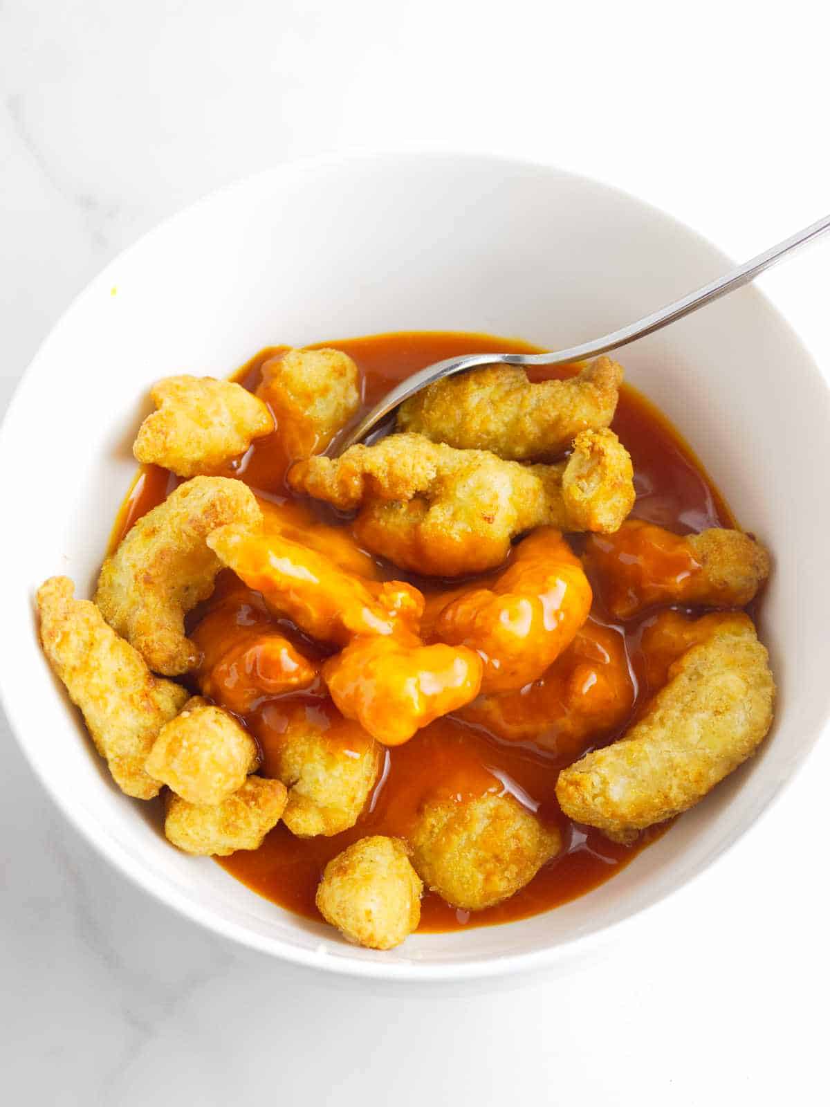 crispy tempura nuggets in a bowl with sauce, being tossed.