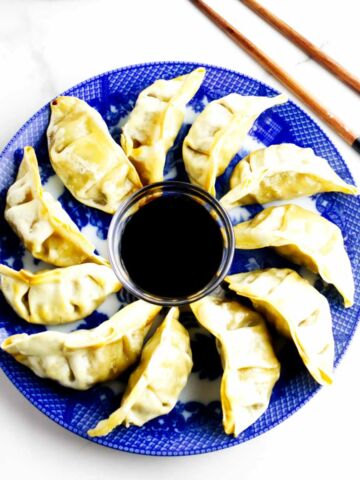 platter full of pot stickers with soy sauce dip in the middle and chop sticks nearby.
