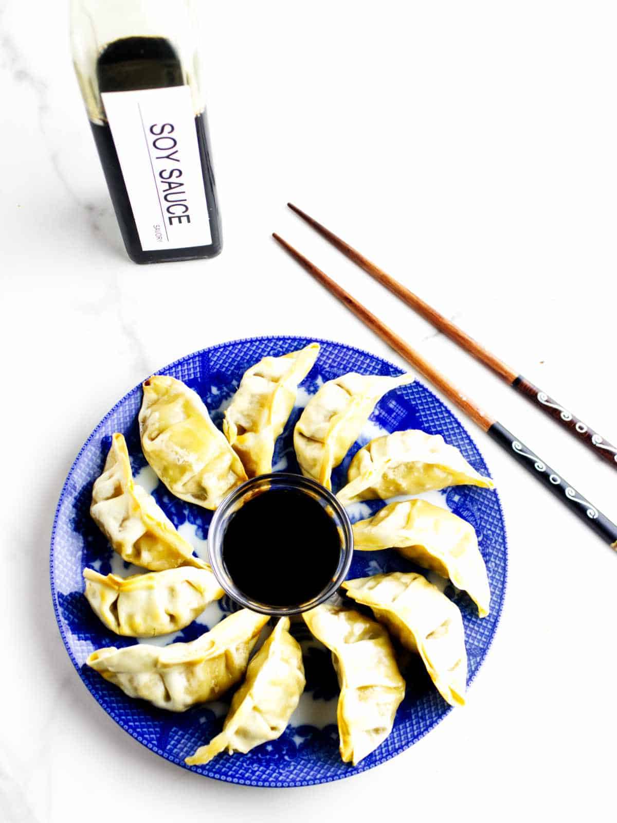 platter full of air fried pot stickers with soy sauce dip in the middle and chop sticks nearby.