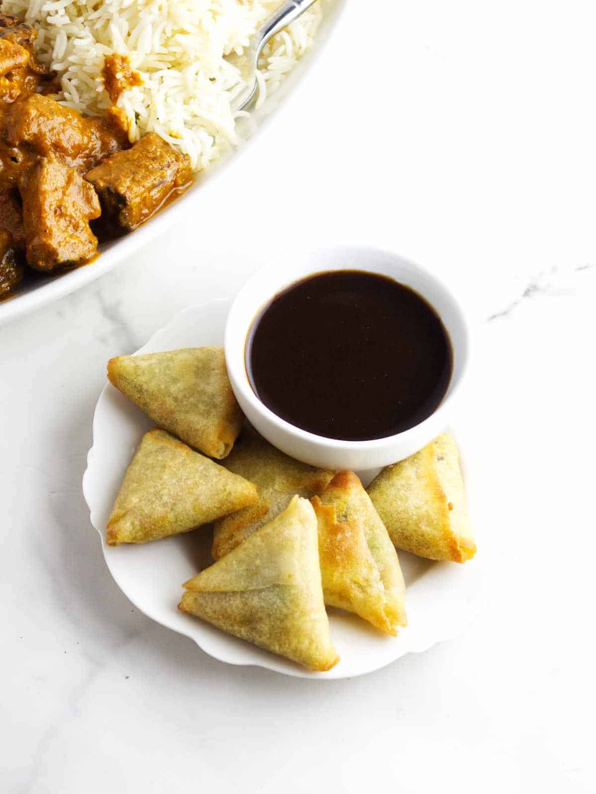 air fried samosa appetizers with dip and platter of rice and curry.
