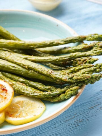 Air fryer asparagus and grilled lemon slices on a blue plate, set against a light blue background.