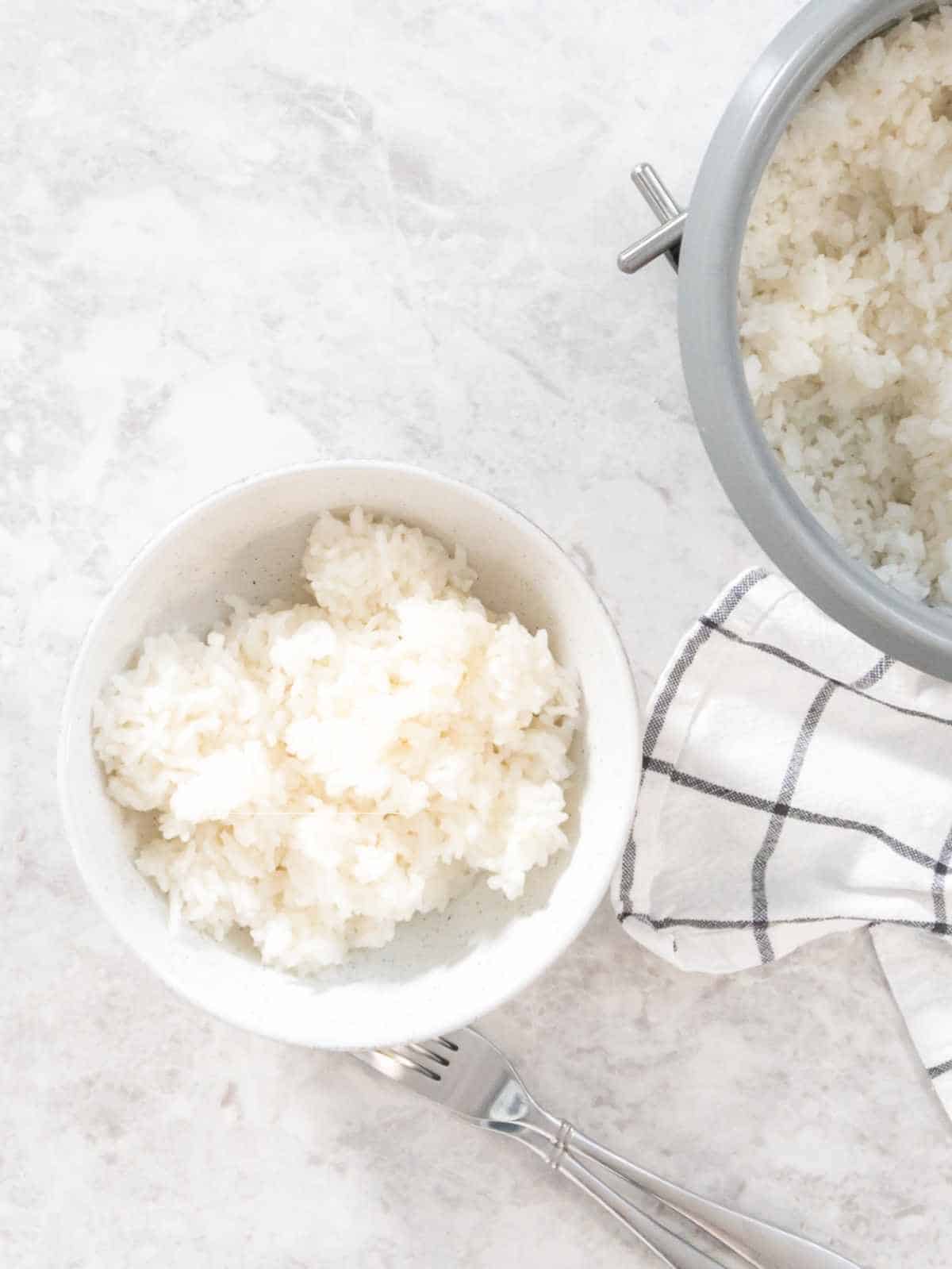 fluffy rice on a wooden spoon over a rice in a bowl with a napkin nearby.