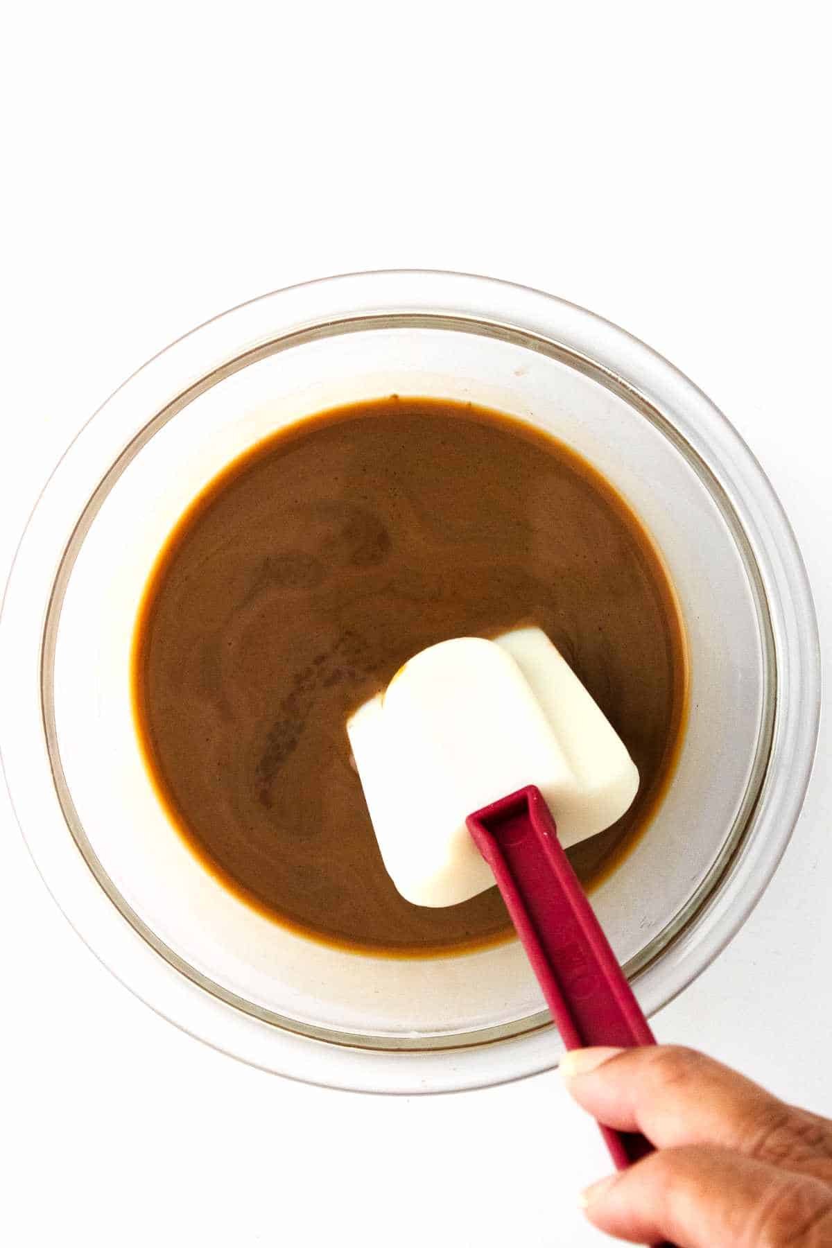 clear glass bowl with white spatula stirring irish cream into melted chocolate.