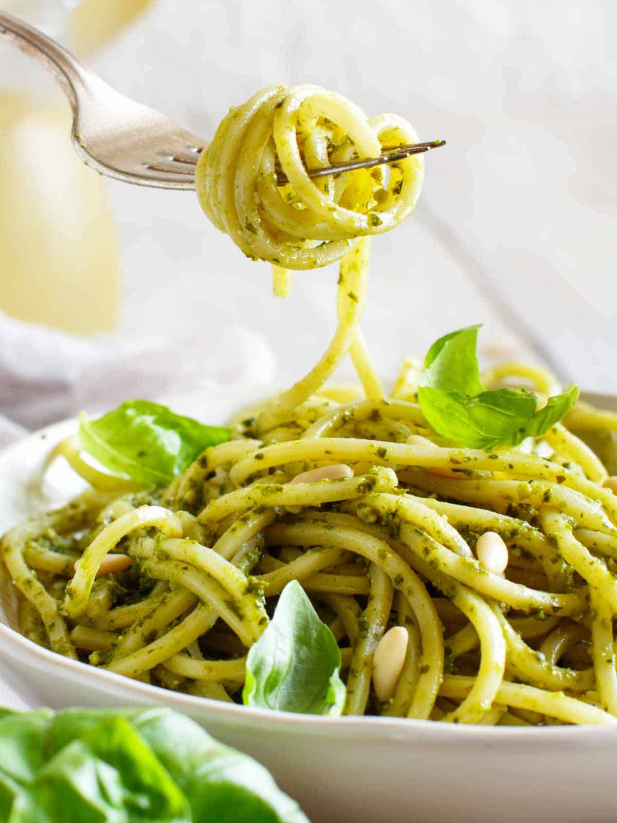 spaghetti with green pesto sauce on a plate with a fork twined with a bite of noodle and pesto mix.