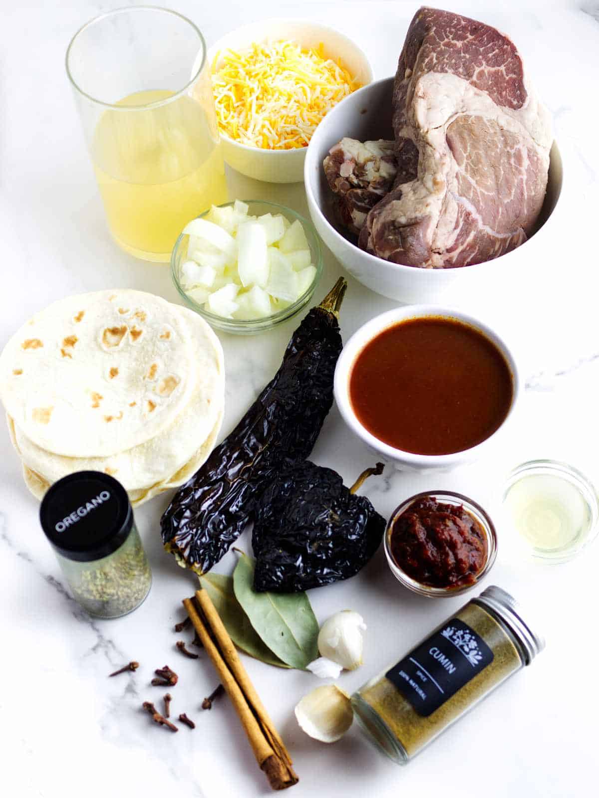 Ingredients for birria quesadilla including beef, dried chiles, spices, tortillas, and cheese.