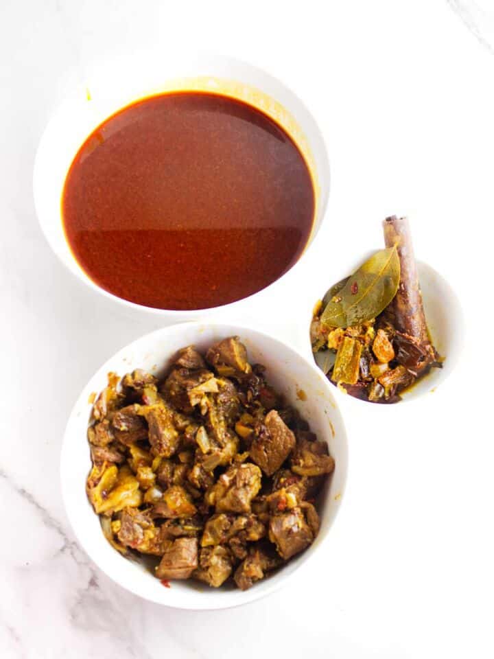 Cooked birria beef, consome, and aromatics separated into bowls.