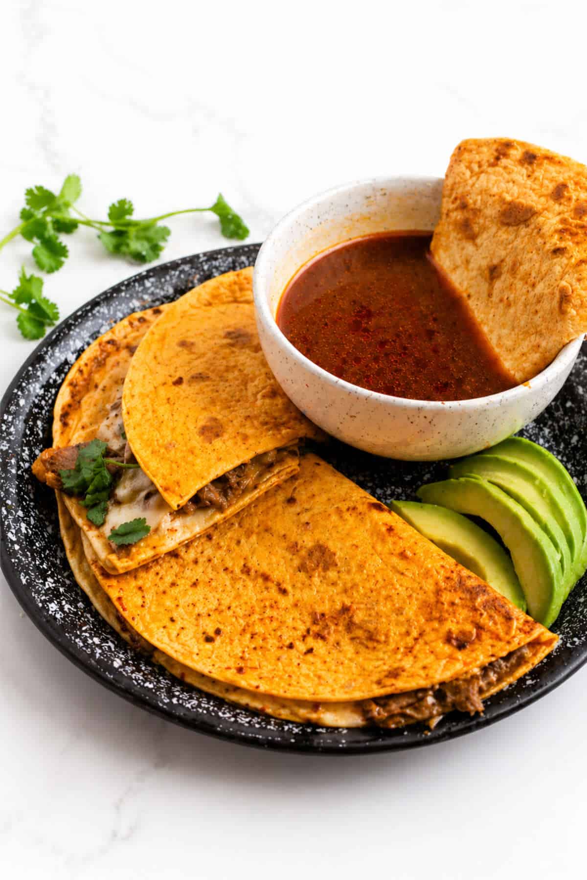 Birria quesadilla served with dipping consome and fresh cilantro garnish.