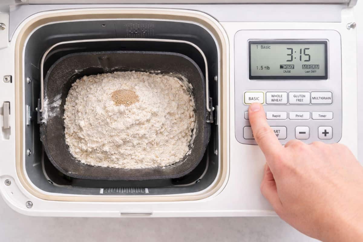 A ball of bread dough sits in the nonstick pan of a bread machine, with some flour and dough residue on the sides of the pan.