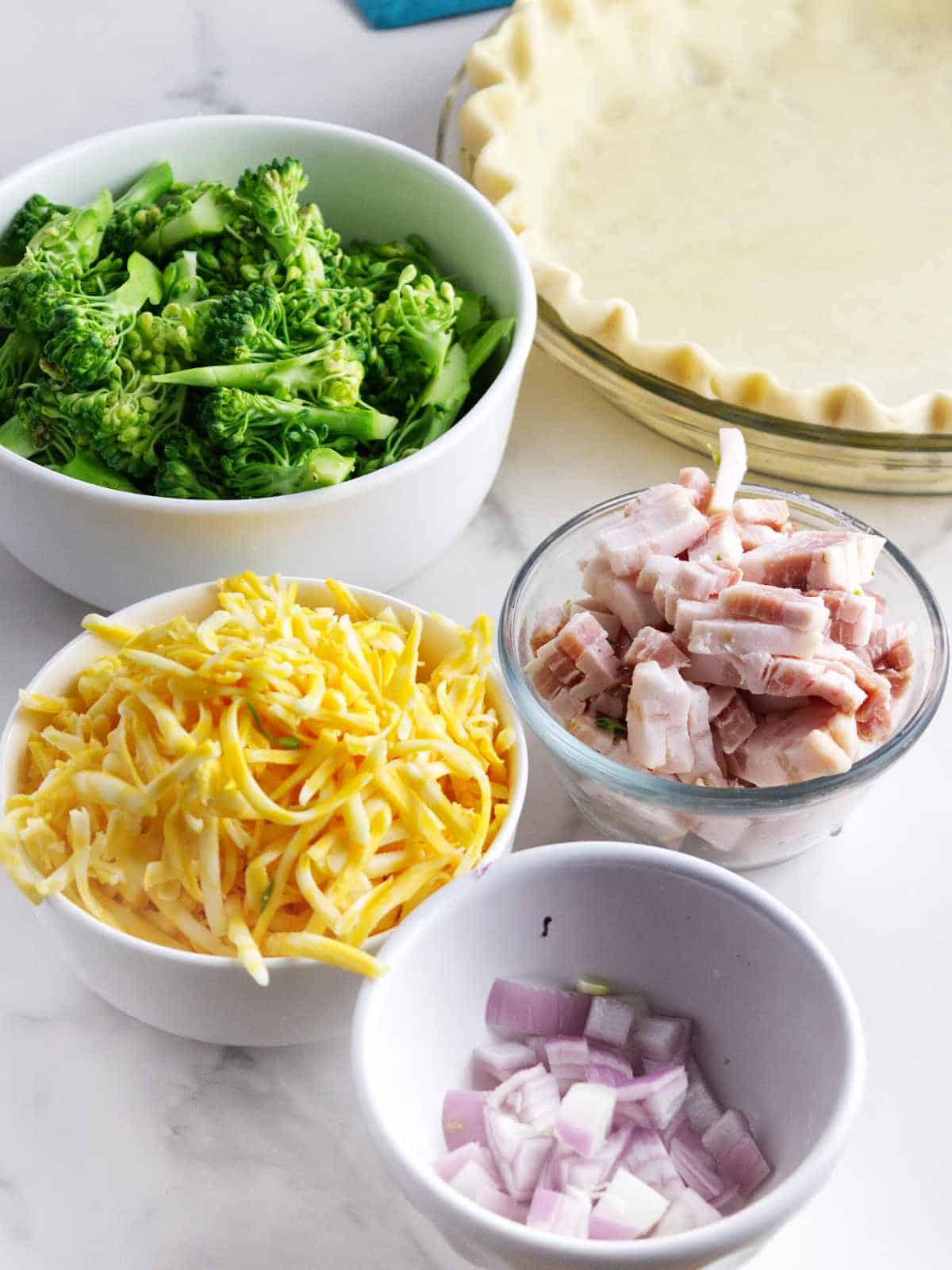 broccoli, cheese, shallots, and bacon fillings and a pie crust in a pie pan.