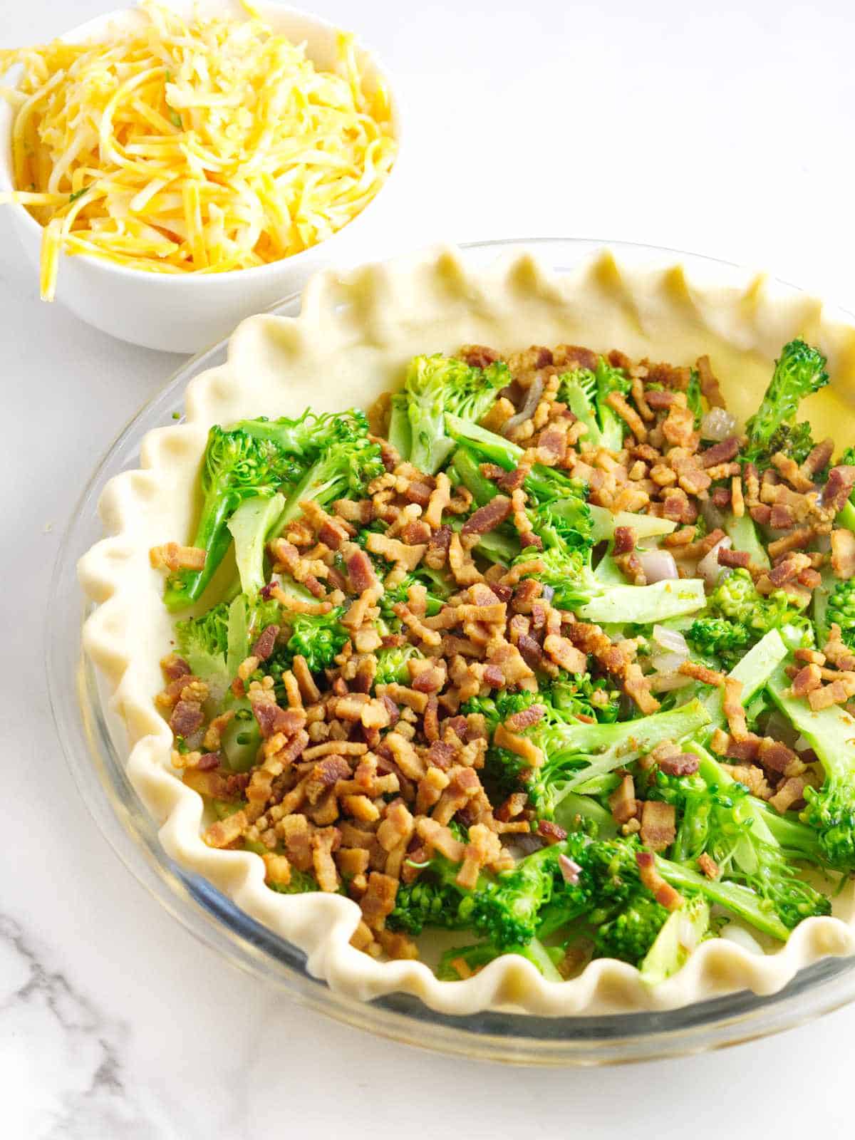 broccoli and bacon in a pie crust with cheese nearby.