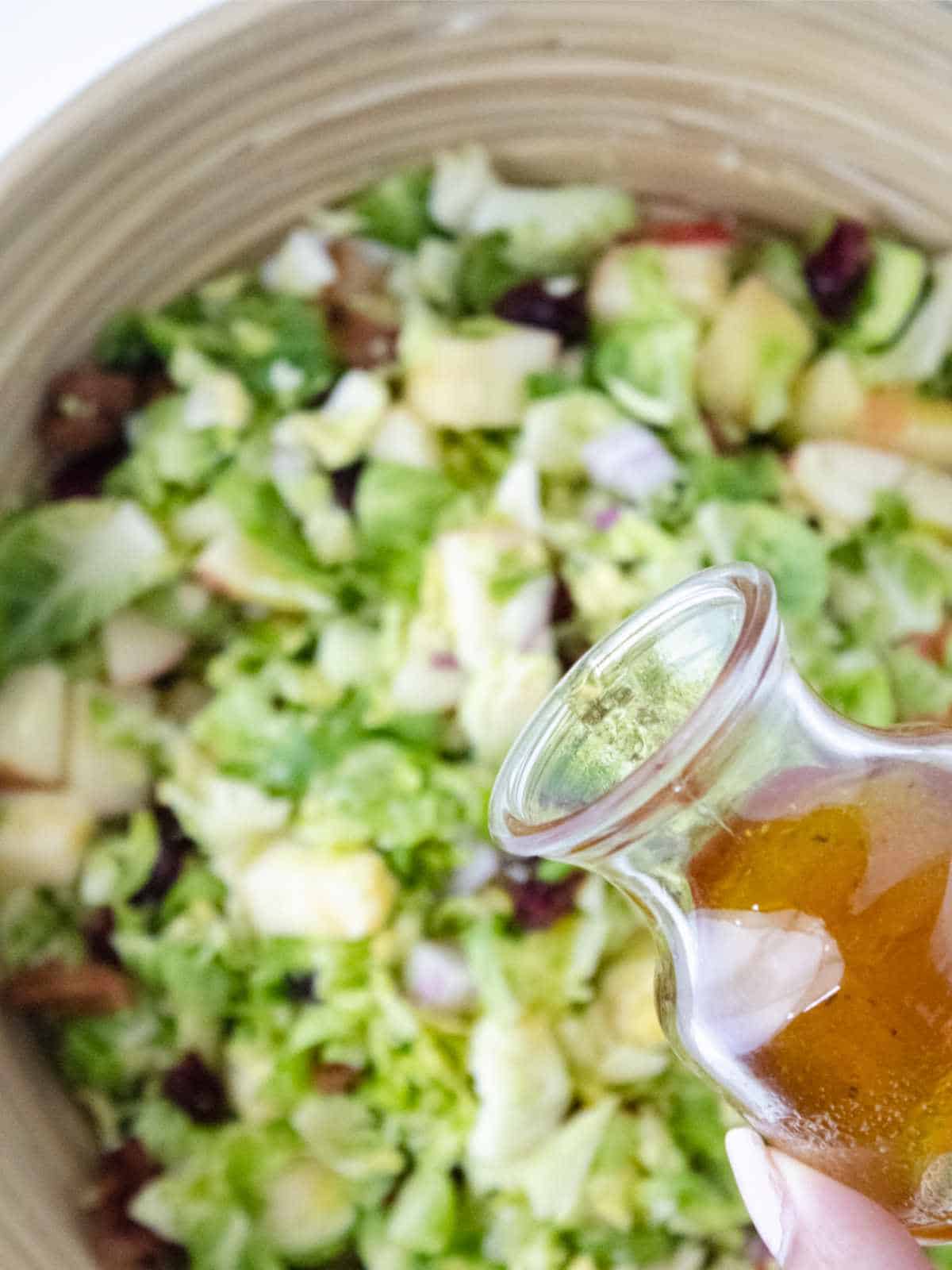 pouring warm salad dressing on brussel sprout salad.