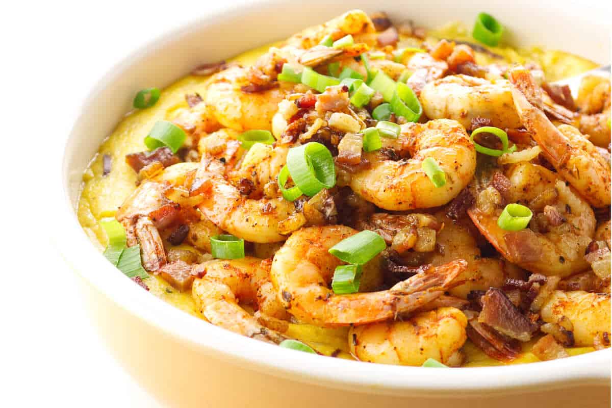 Casserole dish of blackened shrimp on grits garnished with green onion.
